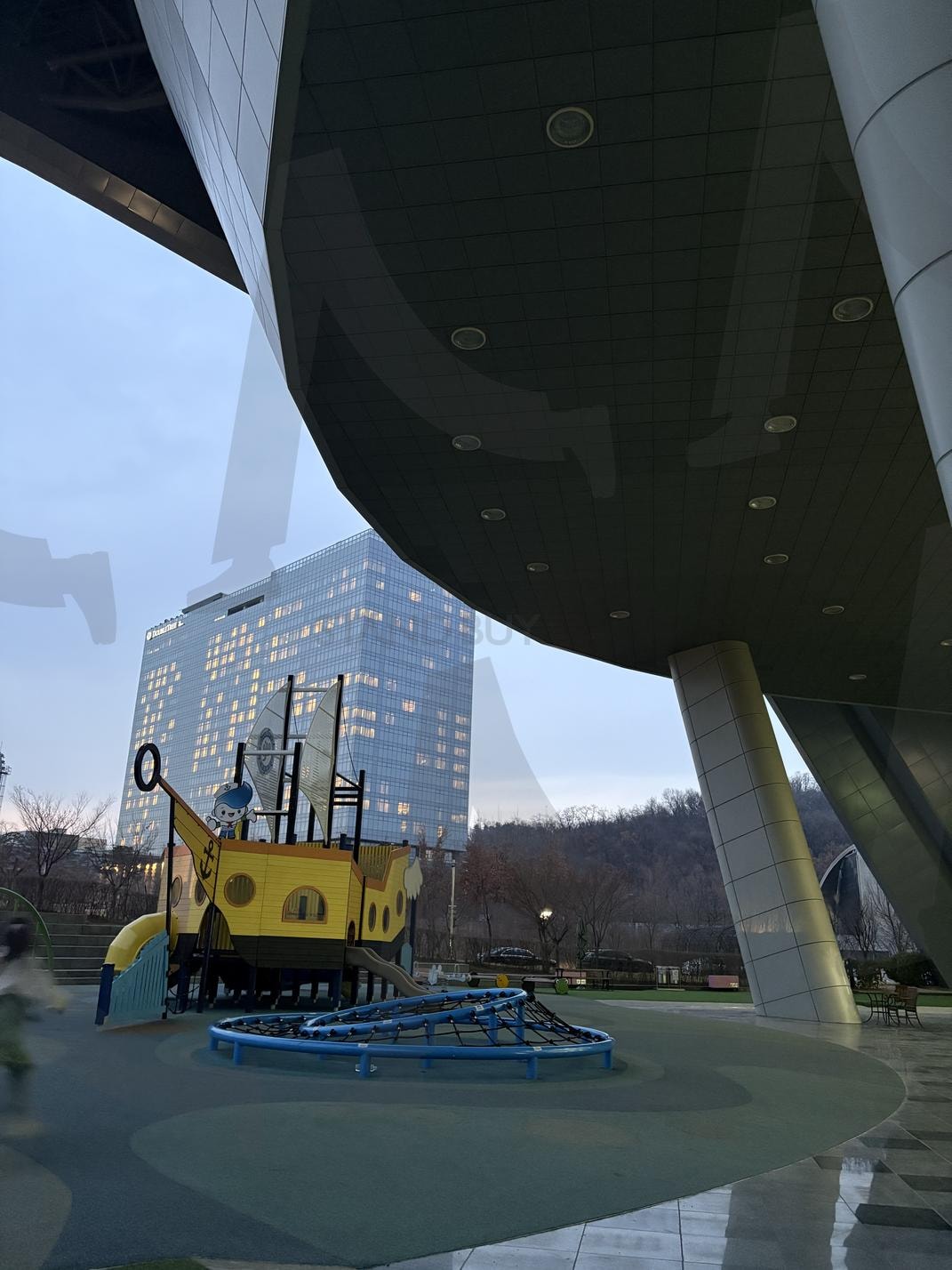 Playground Under the Futuristic Structure | playground, Modern Architecture, urban space, ship-themed play structure, futuristic design, public park, children’s play area, outdoor recreation, cityscape, interactive environment. | 스탠바이 STANDBUY 디지털 콘텐츠