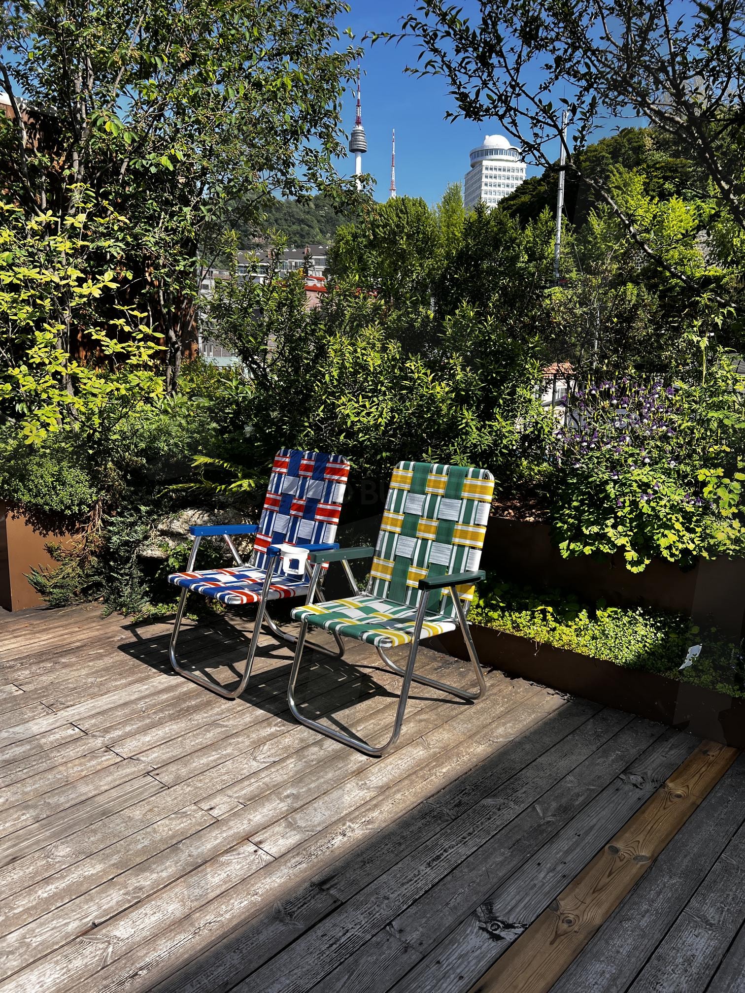 나무 데크 위의 두 개성 있는 캠핑 의자와 서울타워 | 캠핑 의자, 접이식 의자, 나무 데크, 서울타워, 풍경, 야외, 휴식, 여름, 햇살, 정원 | 스탠바이 STANDBUY 디지털 콘텐츠